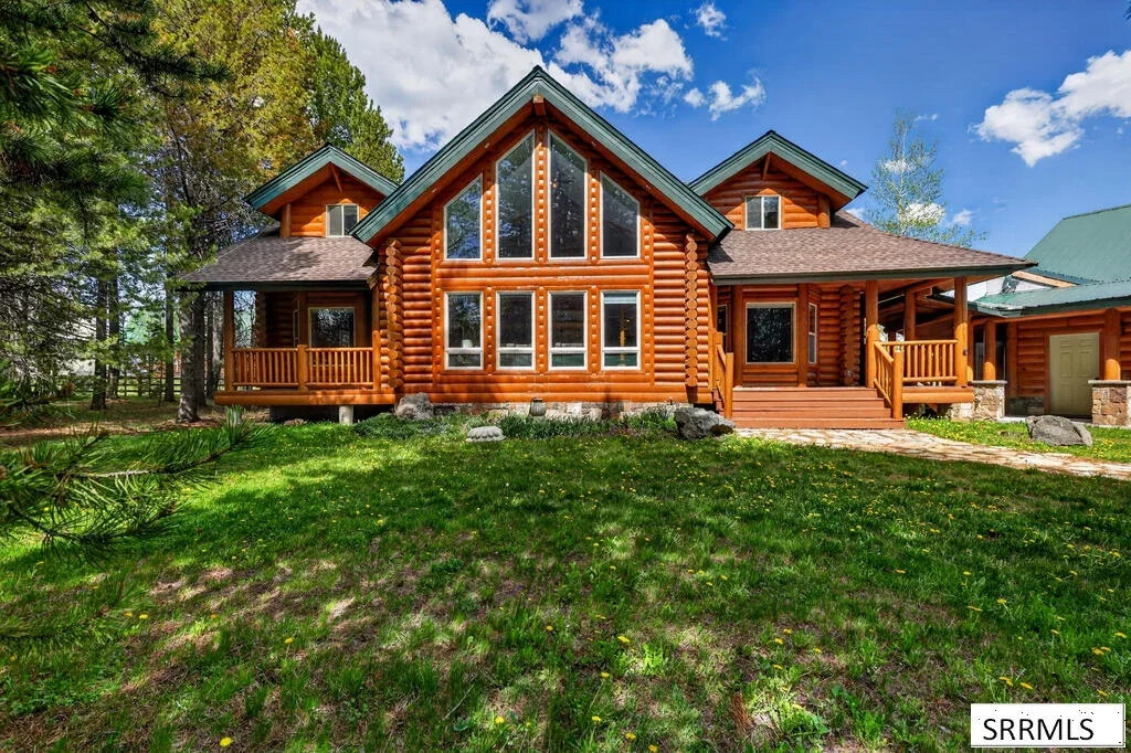 A log home with a covered porch, evergreen trees, and a landscaped lawn in East Idaho